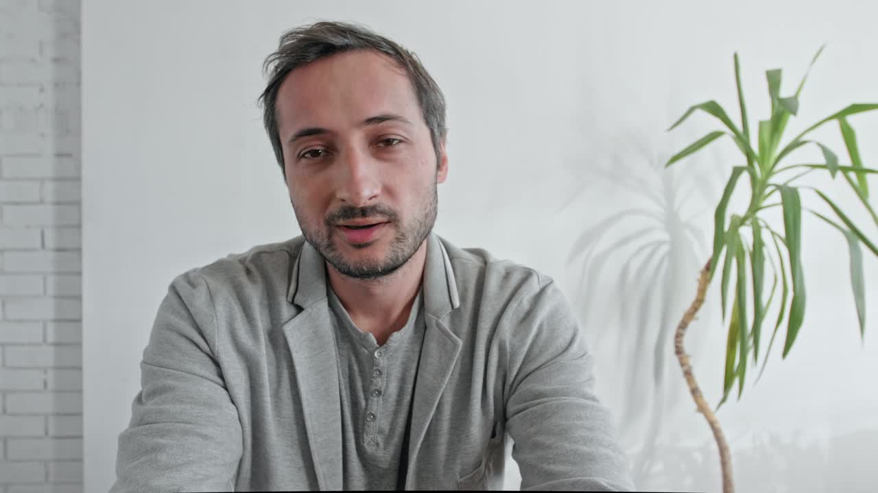 hombre cansado blogueando contra el fondo de una pared blanca y una planta verde