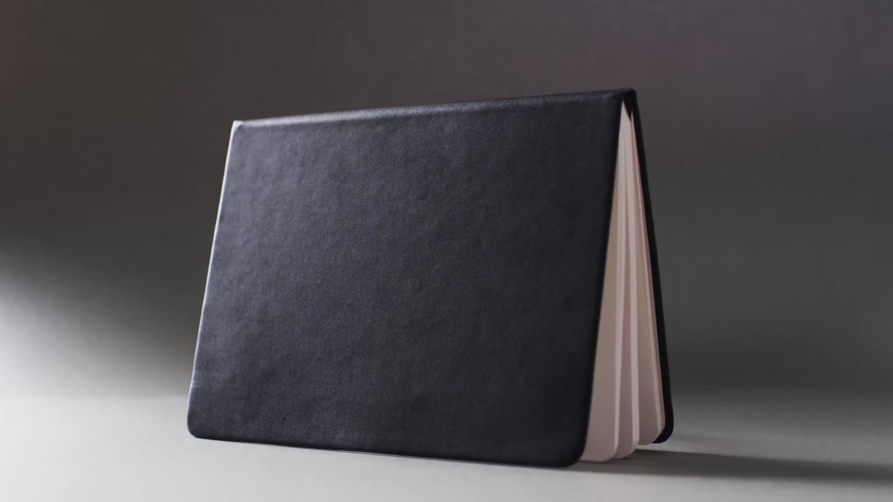 Close up of open black book standing horizontal with copy space on gray background in slow motion