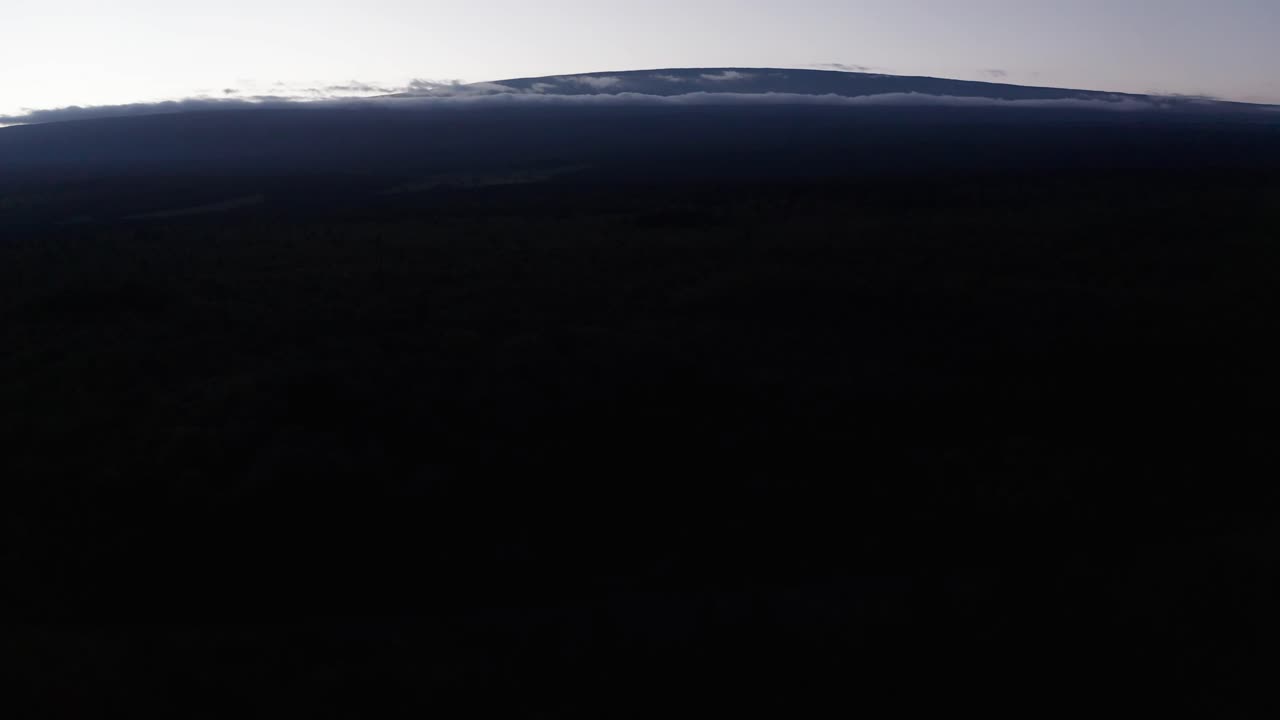 Aerial close-up tilting up shot of Mauna Loa peeking above the clouds at sunset on the island of Hawai'i