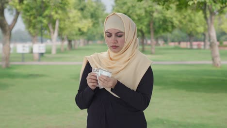 sad muslim woman counting money in park