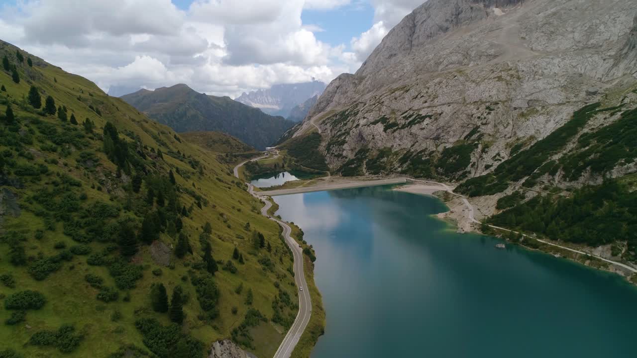 Aerial, drone shot, over a lago di fedaia, following a road, on Marmolada mountain, on a sunny, summer day, at Fedaia pass, in Dolomiti, Tyrol, Italy