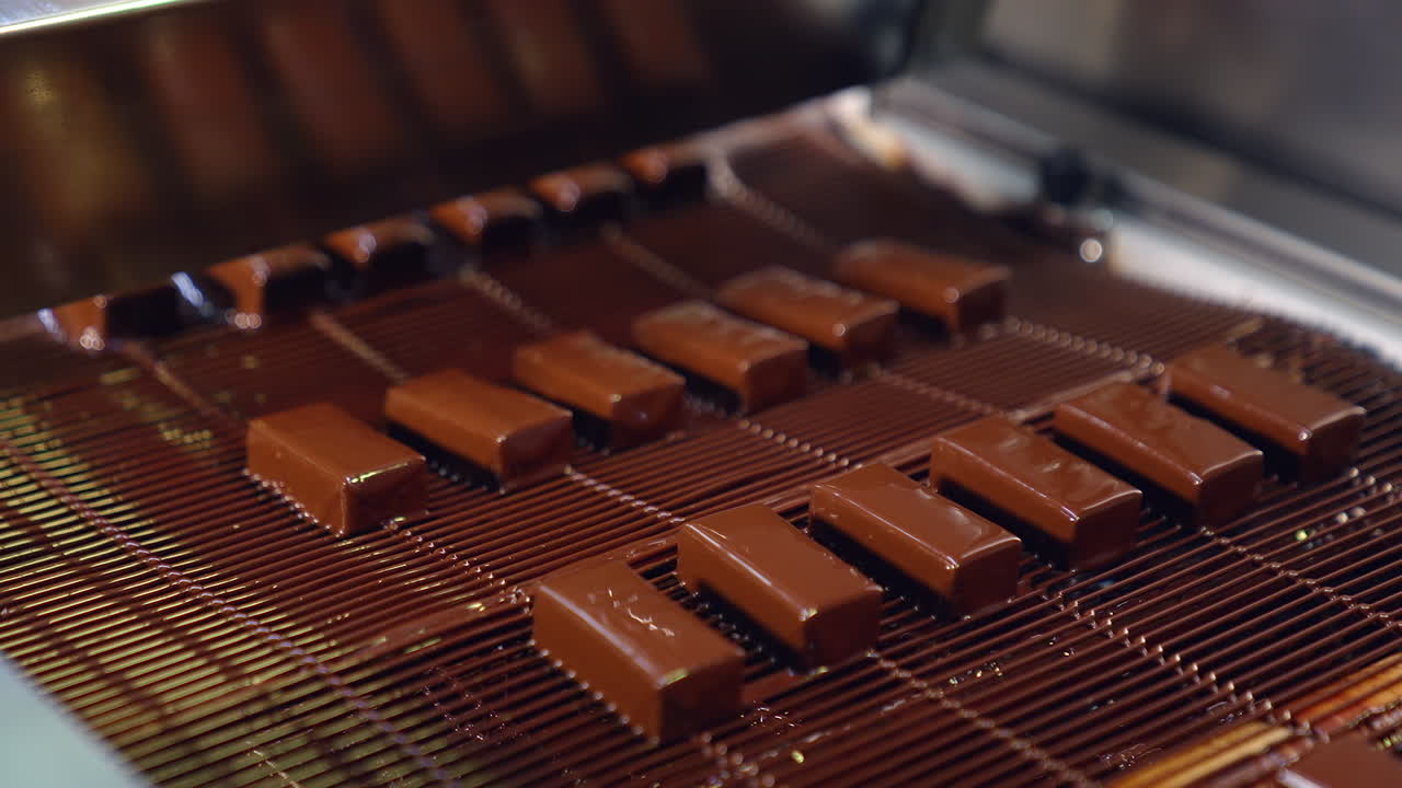 Pouring chocolate at a candy factory for the production of chocolates. Sweets are poured with chocolate on production line at a candy factory close up.
