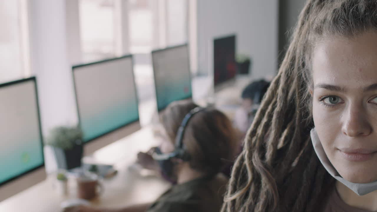 Donna con dreadlocks e mascherina in un ambiente di lavoro moderno.