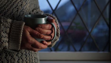 Woman-warming-hands-on-hot-drink-in-window-medium-shot