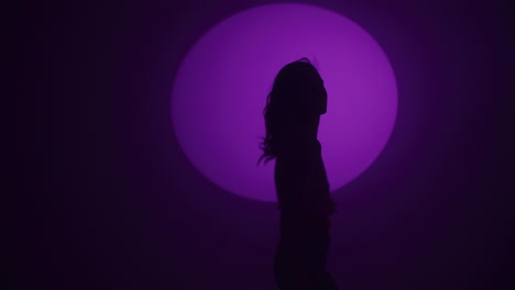 silhouette of a woman dancing under a purple spotlight