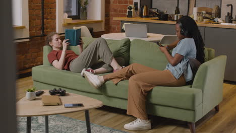 y chicas leyendo un libro y escuchando música con un smartphone en el sofá de casa 1