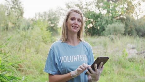 Caucasian-woman-smiling-and-looking-at-camera-with-a-tablet-during-river-clean-up-day