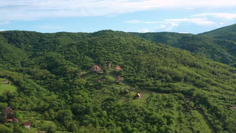 Hermosa-Vista-De-Colinas-Verdes-Cubiertas-De-árboles-Que-Rodean-Un-Pequeño-Asentamiento-Con-Casas-De-Techo-Naranja---Toma-Aérea-De-Drones