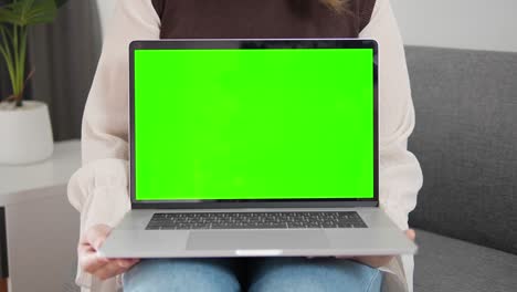 laptop de presentación de mujer con pantalla verde en el sofá en casa
