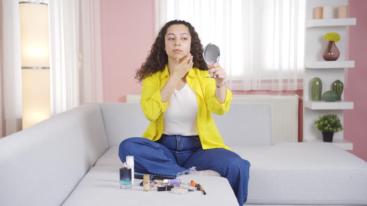 젊은 여자가 그녀의 피부를 보고 있습니다. 그는 거울에 자신을 검사합니다.