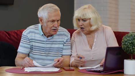 senior old couple stressed about paperwork discuss unpaid bank debt holding bills check expenses