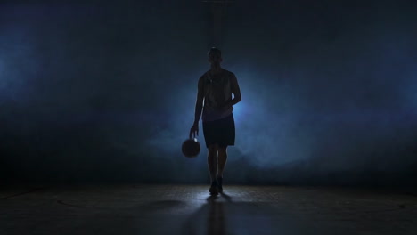 basketball player goes straight to the camera in a dark room with a backlit back in the smoke looking at the camera in slow motion. steadicam