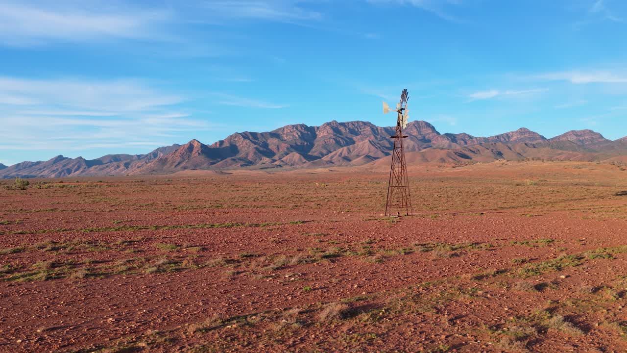 Wide pan orbit around windmill with red dirt and Flinders Ranges mountains in background, South Australia