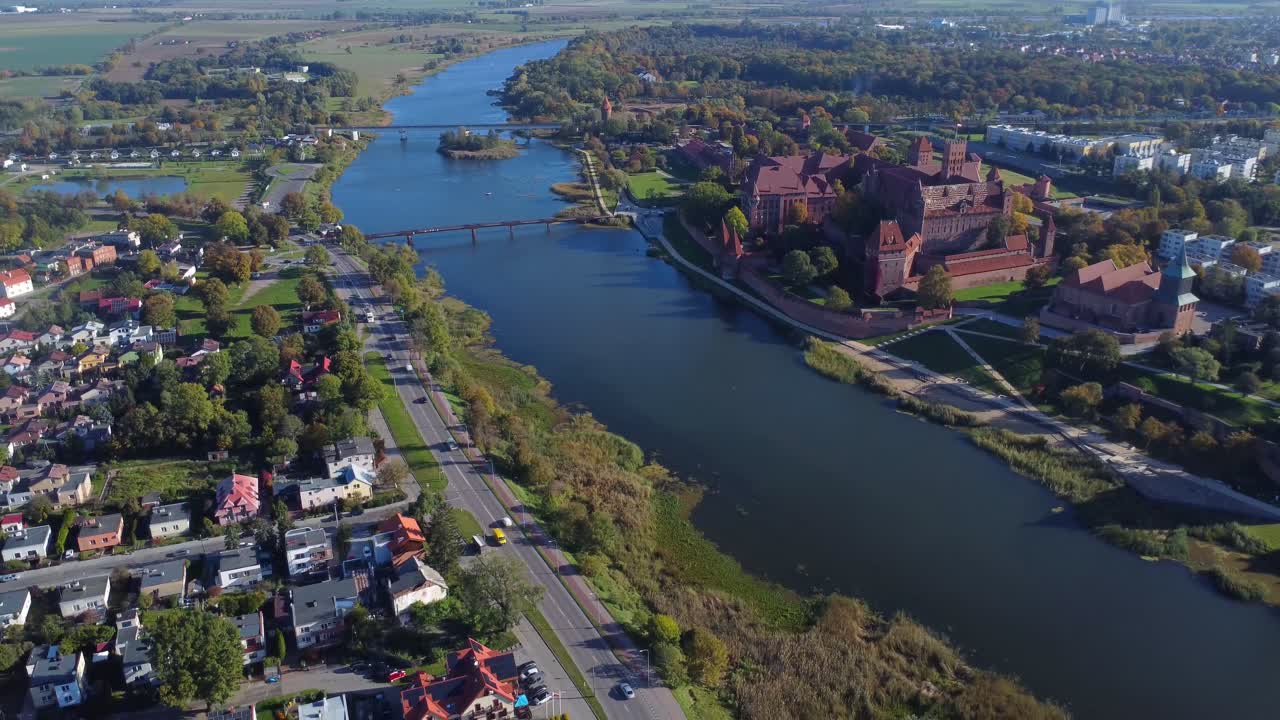 Gothic red-brick Malbork Castle on other side of Nogat River with road and cars passing by - Malbork, Poland