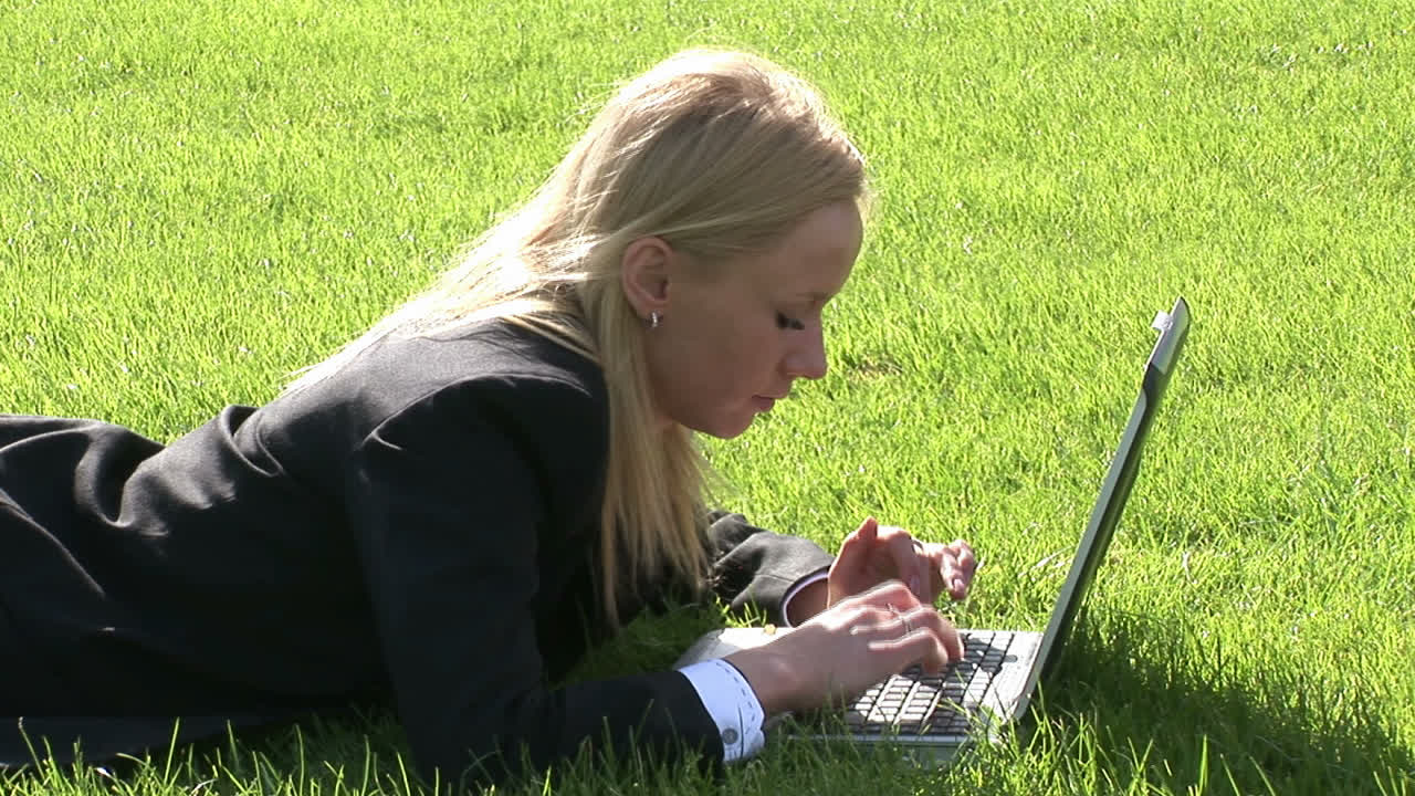 Woman lying on grass using laptop computer