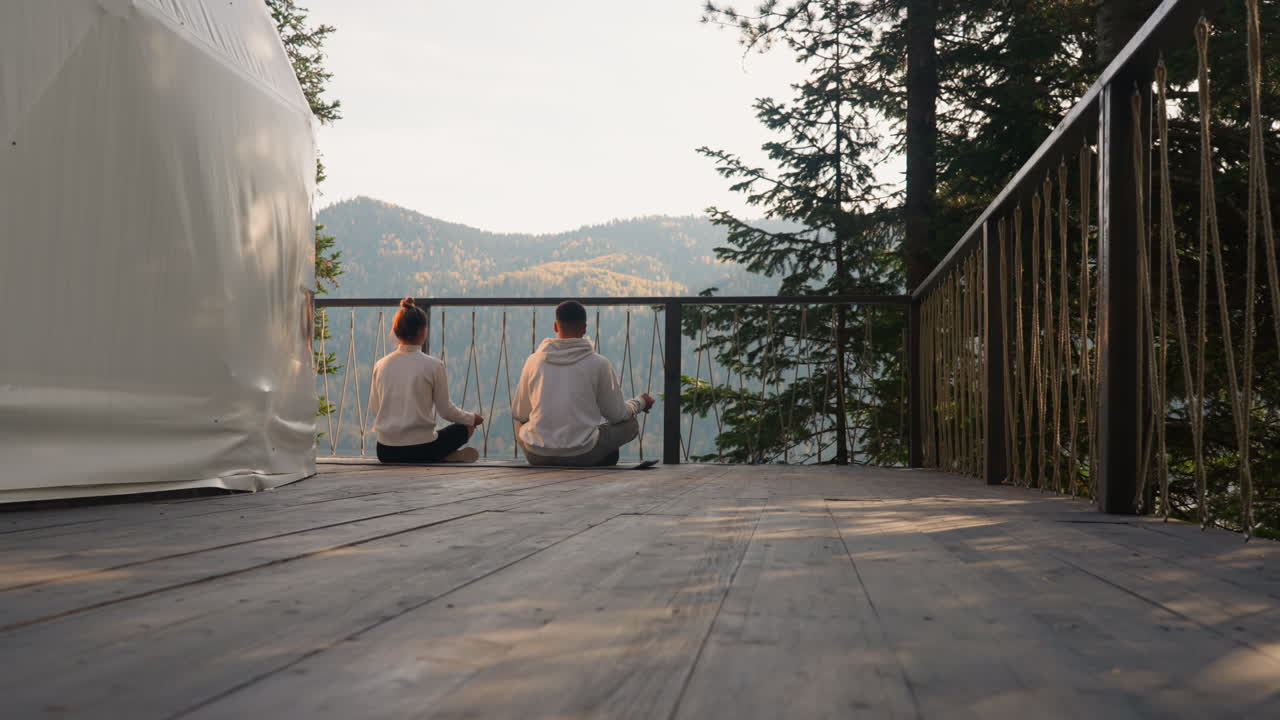 Par mediterer nær glamping-rundtelt. Unge sidder på måtte og dyrker yoga ved søen en forårsmorgen. Konceptet om at finde indre balance.