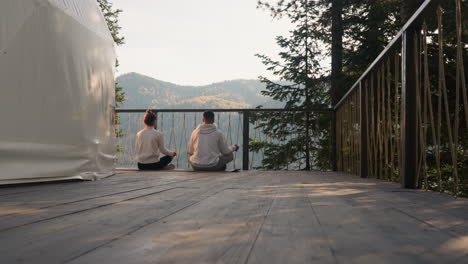 couple meditates near glamping round tent. young people sit on mat practicing yoga by lake in spring morning. concept of finding inner balance practice