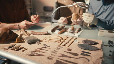 labeled artifacts on lab table, archaeologists discussing skull in background