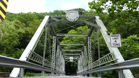 people and a dog riding a bike over a steel truss bridge surrounded by forest