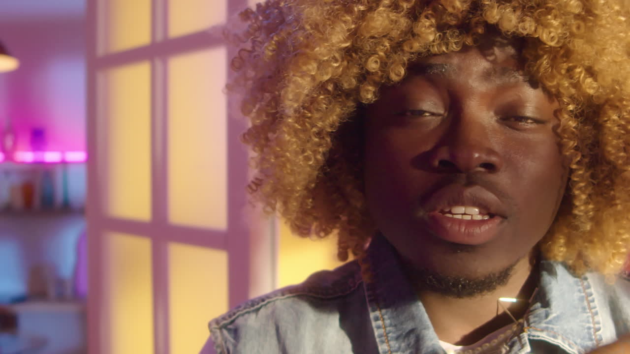 Man with blonde wig and denim jacket in a brightly lit room