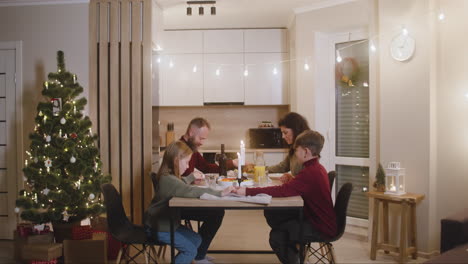 couple and their children pray and bless the table before christmas family dinner 1