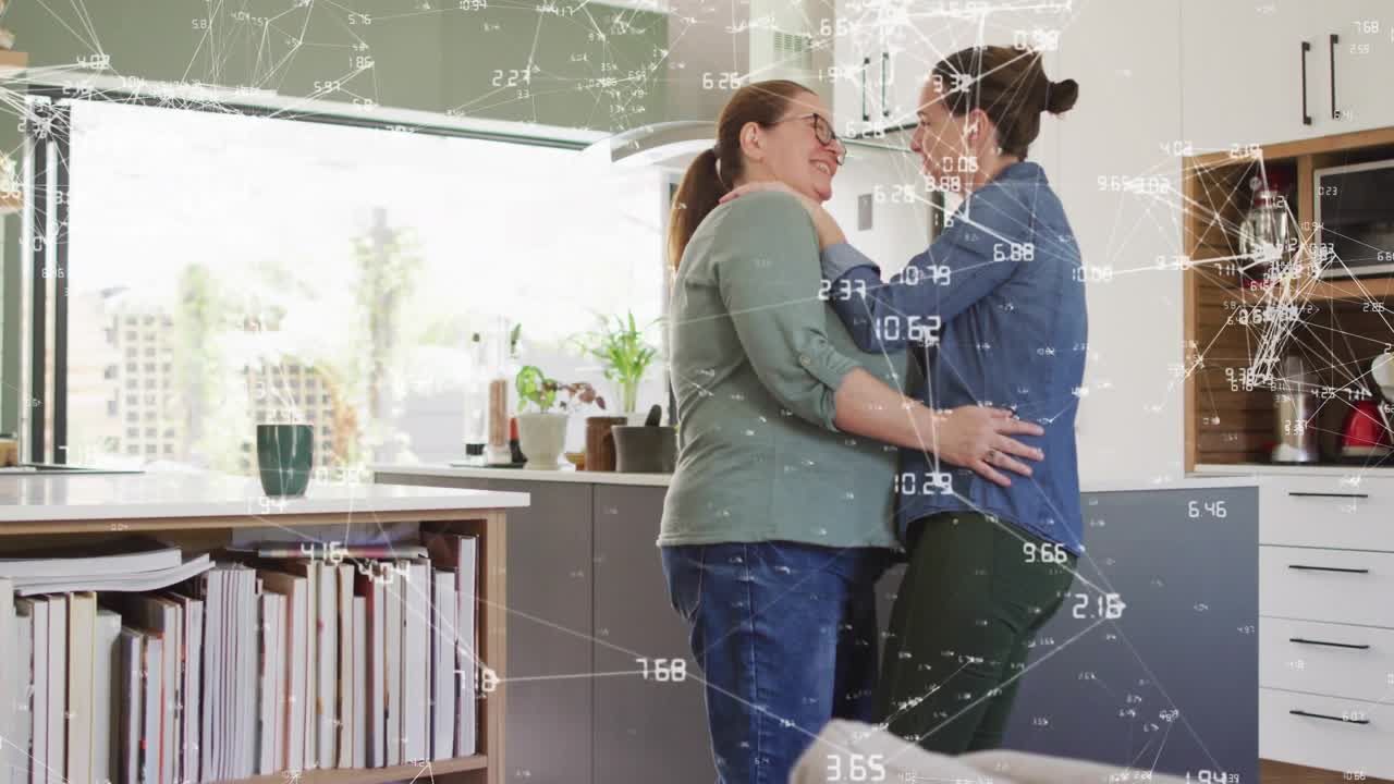 Two women stepping closer and hugging in kitchen, animated network overlay showing connection tech
