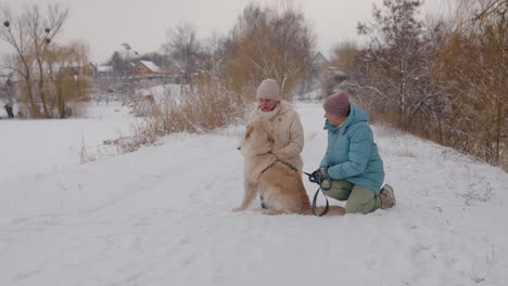 two women walking their golden retriever dog in the snow