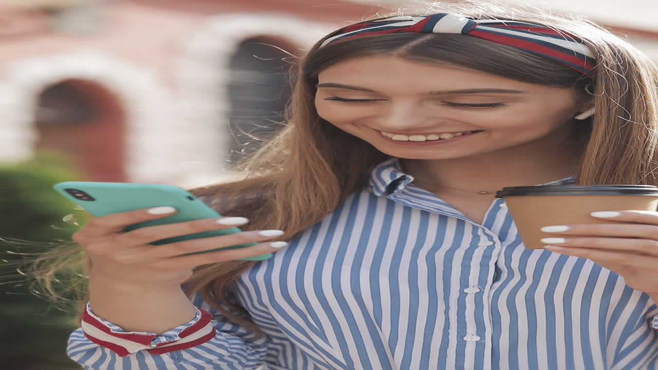 Giovane donna felice che sorride mentre usa lo smartphone e tiene in mano un caffè.