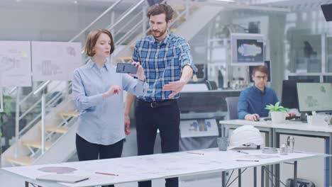 en la instalación de ingeniería industrial: diseñadora con ingeniero jefe utiliza teléfono inteligente para aplicación de realidad aumentada para manipular borradores técnicos de diseño de motores en 3d. oficina de alta tecnología. maqueta