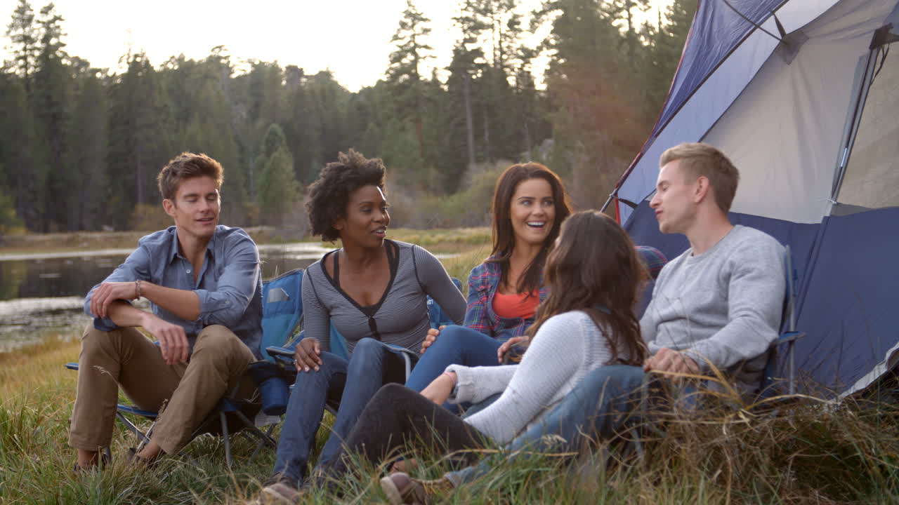 Venner på campingtur som slapper av ved teltet sitt nær en innsjø