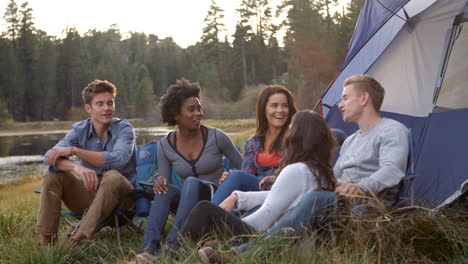 friends on a camping trip relaxing by their tent near a lake