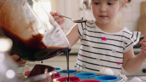 happy little girl helping mother bake in kitchen pouring dough into baking tray preparing homemade cupcake recipe at home