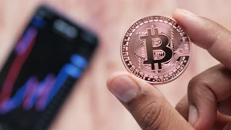 bitcoin coin held in hand with smartphone and financial chart background