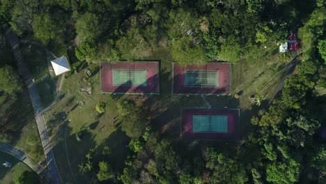 Drohne-Mit-Nach-Unten-Gerichteter-Kamera-Im-Abstieg-Zu-3-Tennisplätzen-Mit-Natur-Im-öffentlichen-Park,-Sport,-Gesundheit,-Freizeit,-In-4K-Auflösung