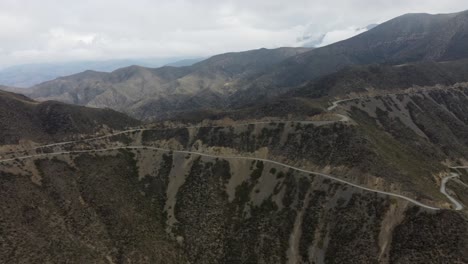 Vista-Aérea:-Camino-De-Tierra-Serpenteante-Que-Serpentea-Por-Un-Paso-De-Montaña-En-Curvas