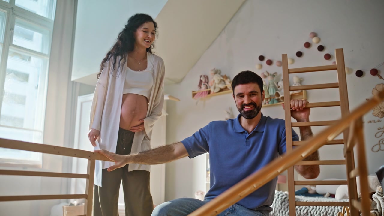 Expectant parents assembling baby crib. Man building furniture pregnant wife.