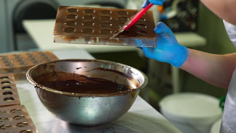 confectioner's hand with spatula in it getting rid of chocolate excesses. spare chocolate is poured into a metal bowl. close up.