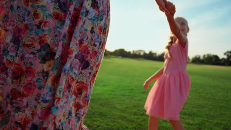 happy family enjoying sunset in city park. woman and girl dancing on meadow.