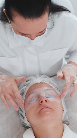 esteticista aplicando una máscara hidratante de regeneración en la piel del rostro de una mujer adulta joven alrededor de los ojos