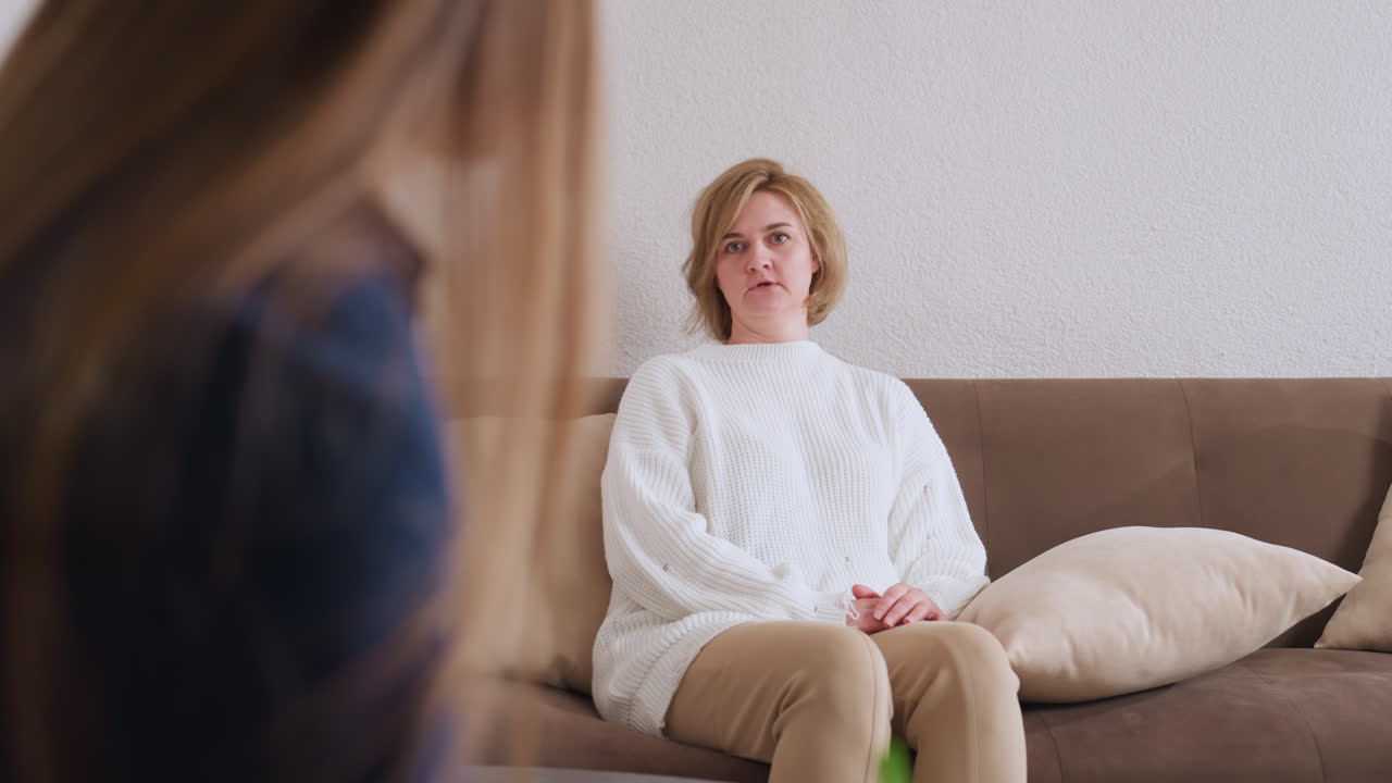 Woman seated on sofa engaged in conversation with counselor, who listens attentively while taking notes, highlighting open dialogue, trust, and emotional expression in calm therapeutic environment