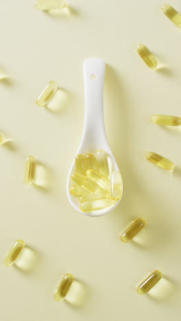 vídeo vertical de cápsulas blancas de cuchara y aceite de hígado de bacalao sobre fondo amarillo con espacio para copiar
