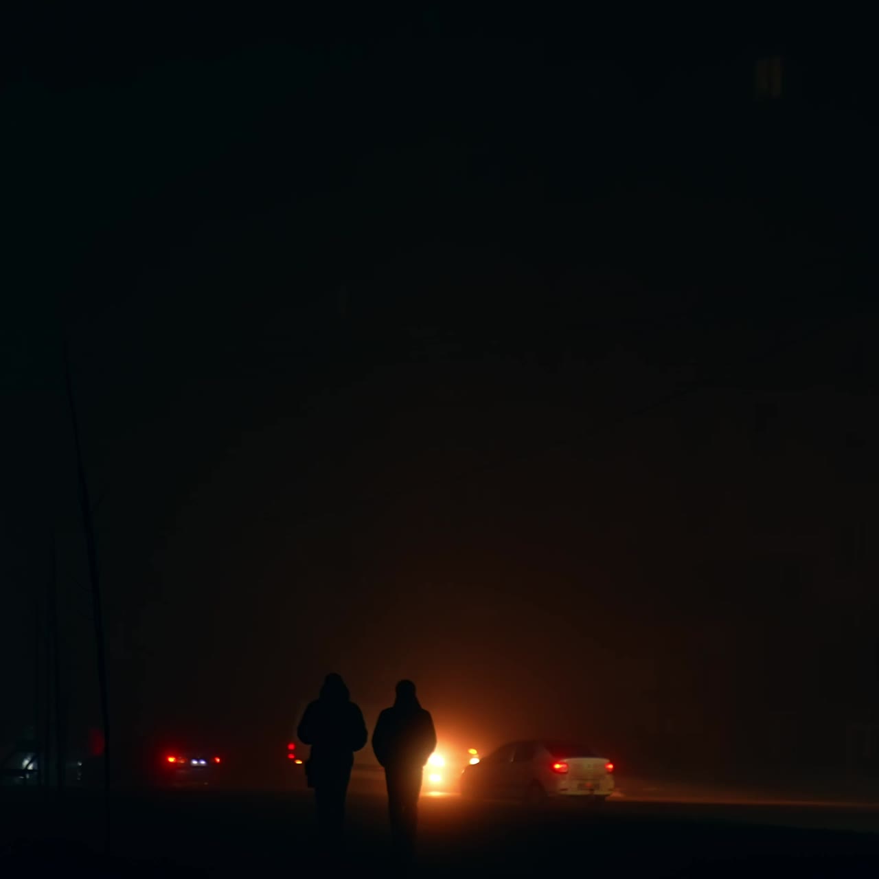 Two dark silhouettes of men walking along the road full of cars. Blackout time in Ukraine after russian drone and missiles attacks. City in darkness from energy outage