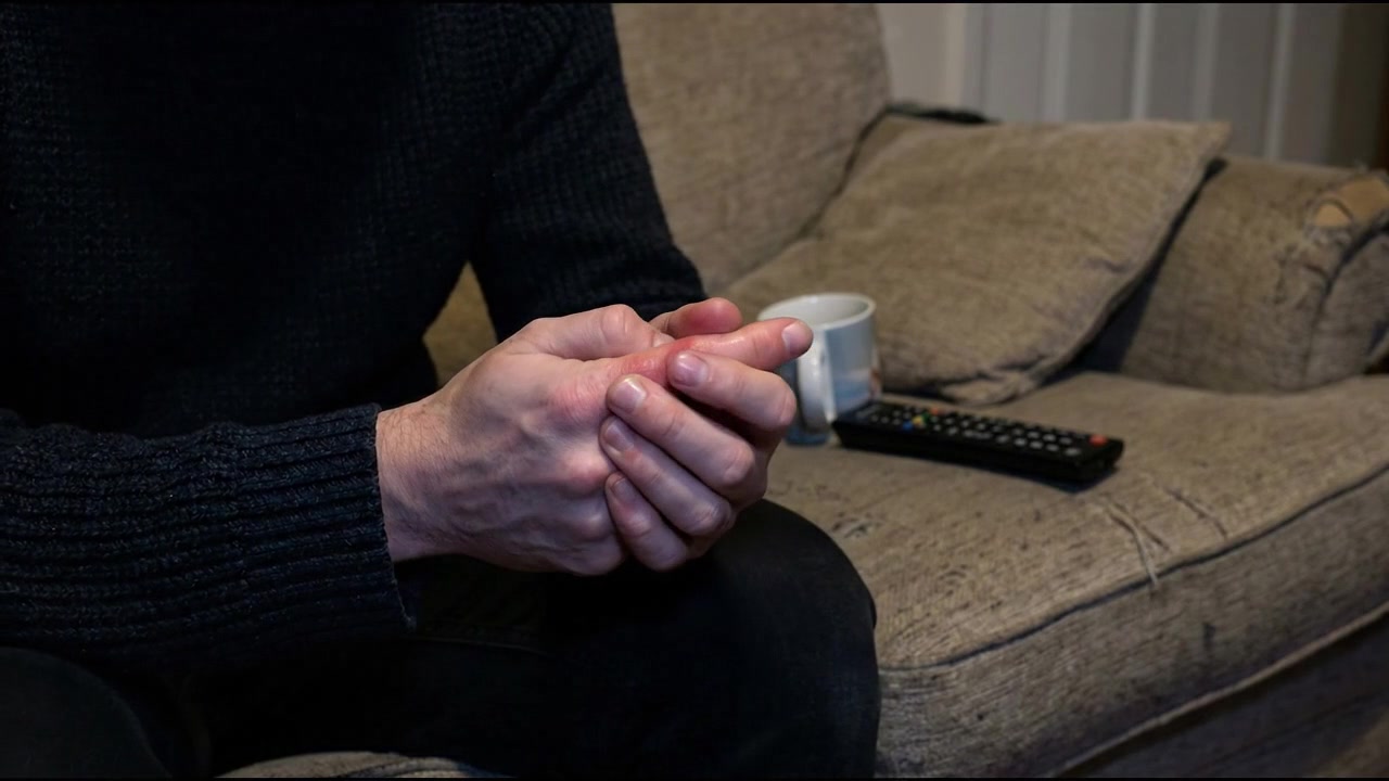 Seated adult supporting painful hand and fingers in dim interior in everyday health concept