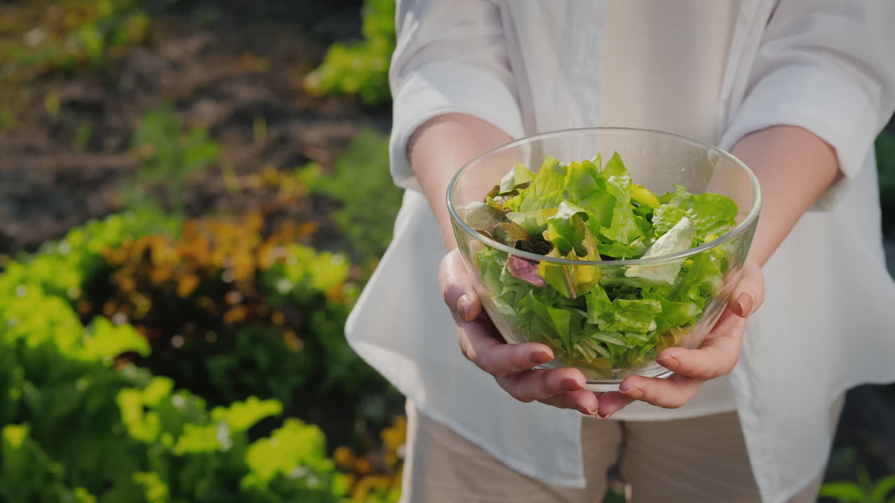 una mujer sostiene un plato de lechuga en el fondo de su jardín
