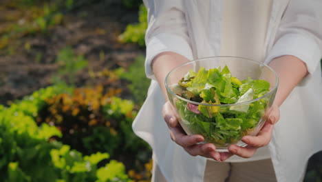 a woman holds a bowl of lettuce on the background of her garden