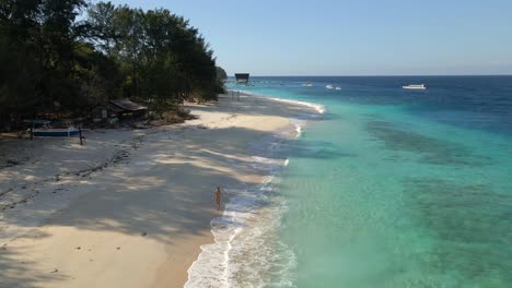 Aerial-tilt-up-view-of-tropical-island-with-crystal-cleat-water-and-person-walking-along-golden-beach