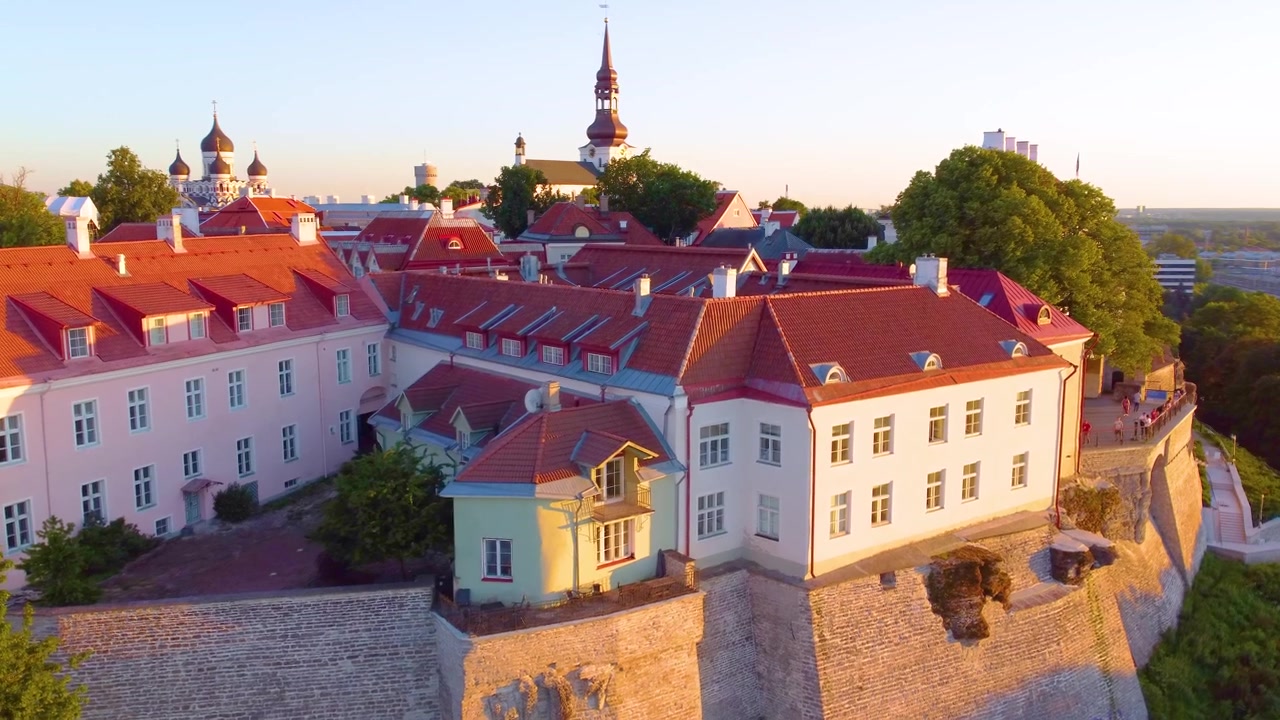 Ilmakuva historiallisesta Tallinnasta, Virosta, kuvattuna kultaisen tunnin aikana. Esillä vanhankaupungin arkkitehtuuria, punaisia kattoja ja rehevää kasvillisuutta lämpimässä iltavalossa.