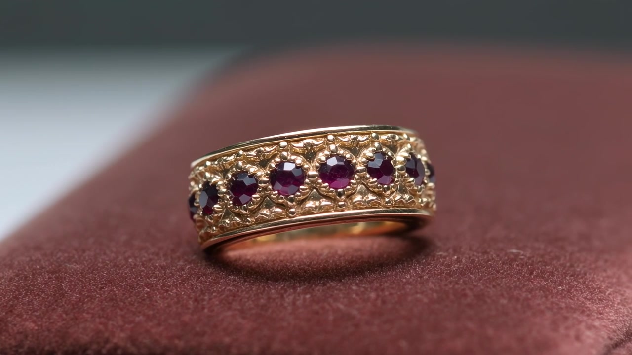 La telecamera si avvicina e ruota un anello d'oro ornato su un cuscinetto di velluto bordeaux, mostrando la filigrana.