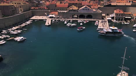 aerial drone flying over the port of dubrovnik, croatia filled with fishing boats and ferrys continuing over the terra cotta rooftops of the walled city and over cathedrals and palaces