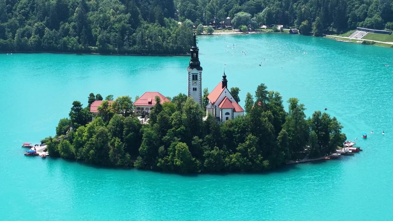 Ripresa con drone dell'Isola di Bled e della Chiesa Cattolica circondati da acqua glaciale blu acquamarina, Slovenia.